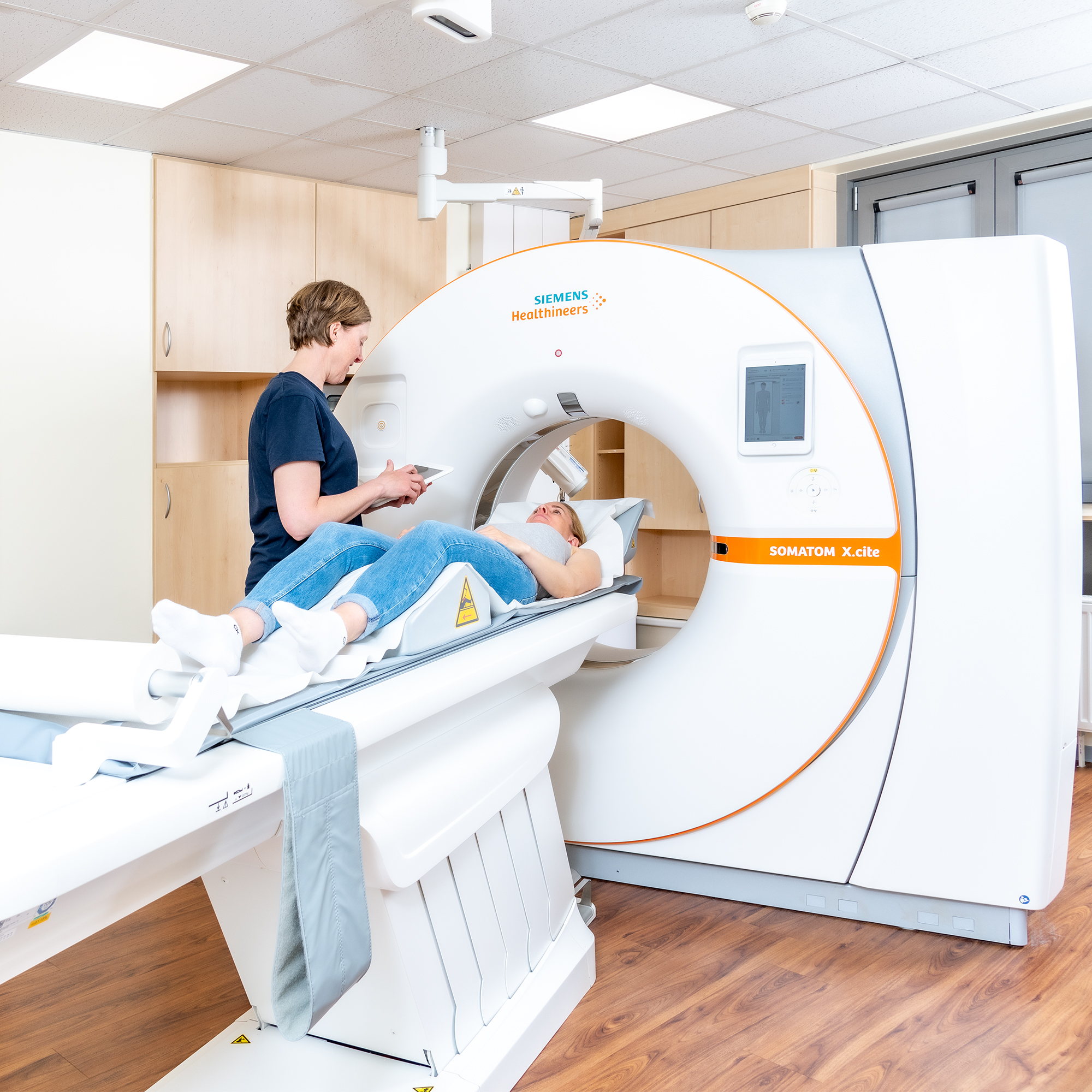 Eine medizinische Fachangestellte stellt Computertomographie ein. Eine Patientin liegt auf der Liege